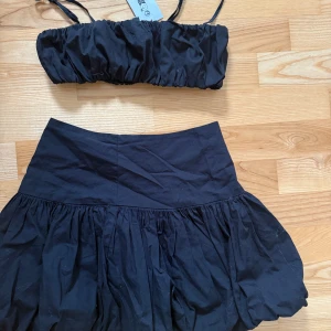 Svart sett med topp och mini kjol från H&M - Svart sett med topp och mini kjol från H&M, med smala axelband och rynkade detaljer. Toppen är ärmlös och har en enkel, stilren design som passar perfekt till sommaren. OANVÄNT 