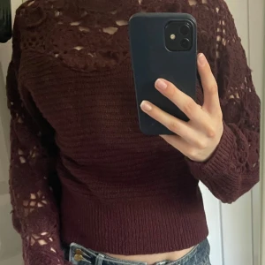 Vinröd stickad tröja med stickade detaljer från Zara - Säljer en vinröd/ lila stickad tröja från Zara med vackra virkade spetsdetaljer upptill och på ärmarna. Tröjan har lång ärm och en croppad passform. Perfekt för dig som vill ha något unikt och snyggt i garderoben! Tröjan är använd en gång.