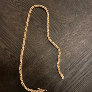 Guldfärgat halsband med kedjemönster - Säljer ett snyggt halsband i guldfärg med ett detaljerat kedjemönster. Perfekt för att lyfta vilken outfit som helst. Längre modell som ger en trendig look.