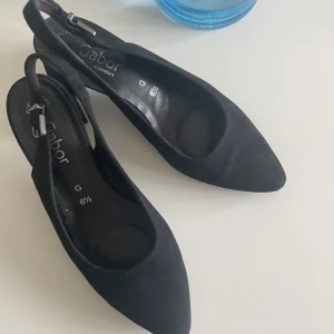 Svarta pumps med klack från Gabor - Säljer ett par svarta pumps från Gabor med rund tå och bred klack. Skorna har justerbar rem med spänne och är tillverkade i mocka. Perfekta för dig som vill ha både stil och komfort. Endast använda en gång av mig så skickat är inget att anmärka på. Kostar 1500 kr i butik nu. 