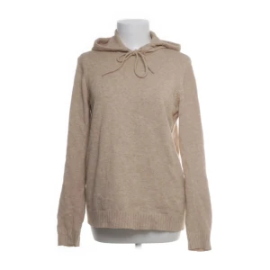 Beige stickad hoodie - Mysig beige stickad hoodie med huva och knytband framtill. Tröjan har långa ärmar och ribbade muddar vid ärmslut och nederkant. Perfekt för lager-på-lager och en avslappnad stil.