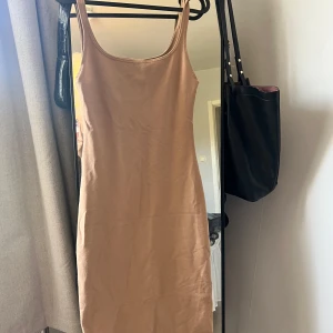 Beige tight klänning från Zara - Säljer en enkel och stilren beige klänning från Zara i storlek S. Klänningen är tight, ärmlös och har en rundad urringning. Perfekt för sommardagar eller att styla med en jacka. Materialet känns mjukt och stretchigt.
