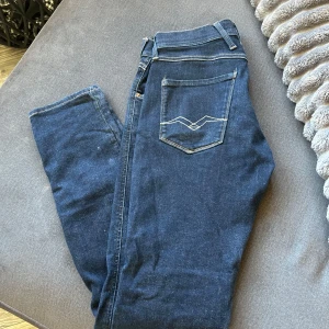Mörkblå Replay jeans strl 30/32 - Säljer ett par mörkblå jeans från Replay med klassisk femficksdesign och snygga kontrastsömmar på bakfickorna. Jeansen har normal passform och raka ben, perfekt för en stilren look. Anbass strl 30/32 