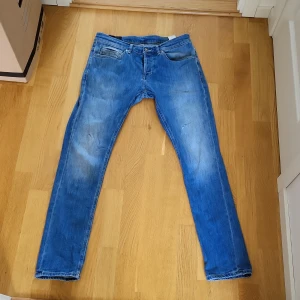 Blå jeans från Dondup - Säljer ett par klassiska blå jeans från Dondup, tillverkade i Italien. Jeansen har fem fickor, raka ben och normal passform. Perfekta för dig som gillar en tidlös stil med snygg tvätt och diskreta detaljer.