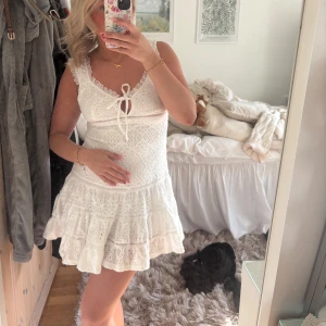 Vit spetsklänning med volang - Supersöt vit klänning i spets med volangkant och knytning framtill. Klänningen har breda axelband och är kort i modellen. Perfekt för sommaren, aldrig använd med lappar kvar 🤍🤍🤍🤍