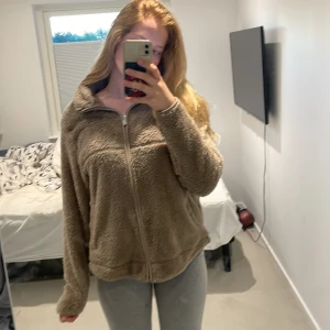 Beige fleecejacka med dragkedja - Mysig beige fleecejacka med dragkedja framtill och hög krage. Perfekt för kyliga dagar och enkel att matcha med olika outfits. Jackan har lång ärm och en avslappnad passform.