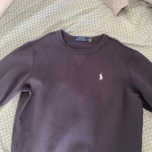 Mörkblå sweatshirt från Polo Ralph Lauren - Mörkblå sweatshirt från Polo Ralph Lauren med klassisk rund halsringning och broderad vit logga på bröstet. Tröjan har långa ärmar och är perfekt för en avslappnad stil. Helt nytt skick riktigt skön