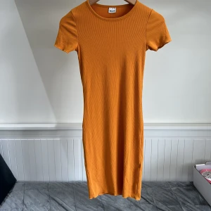 Ribbad orange klänning från Gina Tricot - Säljer en ribbad orange klänning från Gina Tricot i storlek XS. Klänningen har korta ärmar, rund halsringning och är i en mjuk, stretchig bomullsblandning. Perfekt för dig som gillar enkel och stilren design.