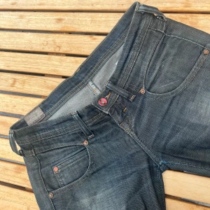Mörkblå jättelågmidjade jeans från Lee - Skitsnygga Lee-jeans som säljs för att de är lite för små för mig. Jag har klippt upp de lite på insidan längst ned på benet för att få de se mer flared ut men inget man tänker på. De passar mig med strl 34 men tror de sitter bättre på strl 32. De är diselfärgade/mörkblåa. Det är w25 L33