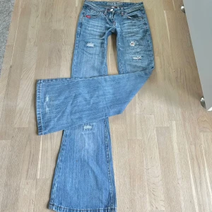 Blå bootcut jeans från Blue Queen - Säljer ett par blå bootcut jeans från Blue Queen med slitna detaljer och patchar. Jeansen har låg midja, klassiska fem fickor och vida ben. Vääärldens snyggaste men måste tyvärr sälja då dom är för små. Små slitningar nere vid benen