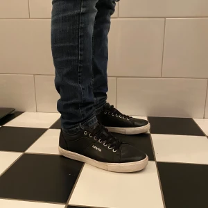 Levi’s skor - Säljer ett par svarta sneakers från Levi's med vit sula och klassisk snörning. Skorna har en stilren design med rund tå och Levi's-logga på sidan. Perfekta för en avslappnad och trendig look.