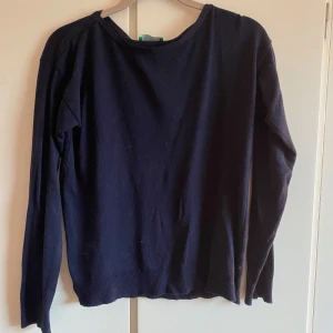 Mörkblå tröja från United Colors of Benetton - En enkel och stilren mörkblå tröja från United Colors of Benetton. Tröjan har rund halsringning och långa ärmar. Perfekt att matcha med jeans eller kjol för en clean look.