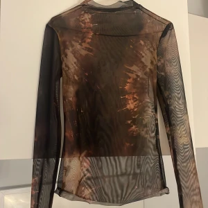 Mesh topp med tie-dye mönster från Zara - Säljer en transparent mesh topp från Zara i storlek S. Toppen har lång ärm och ett coolt tie-dye inspirerat mönster i bruna, svarta och beige toner. 