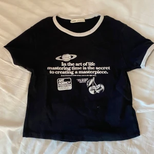 Svart t-shirt med vit text från Pull&Bear - Svart t-shirt från Pull&Bear med vit kontrastkant vid hals och ärmslut. Tryck framtill med text och illustration av planeter. Perfekt för dig som gillar unika prints och bekväma basplagg.