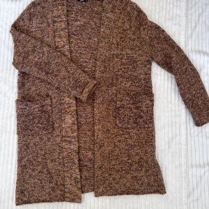 Brunmelerad stickad kofta från Splash - Mysig brunmelerad stickad kofta från Splash med långa ärmar och stora fickor framtill. Perfekt för lager-på-lager och har en avslappnad passform. Snygg att slänga över en t-shirt eller topp.