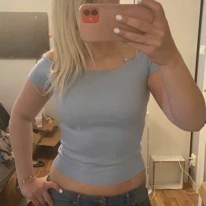 Ljusblå offshoulder topp - Säljer en ljusblå croppad topp med offshoulder-design. Toppen har tight passform och är tillverkad i ett stretchigt material som sitter snyggt på kroppen. Perfekt för varma dagar eller när du vill ha en stilren look.