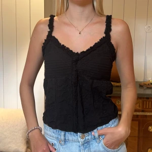 Svart spetslinne med volangdetaljer - Säljer ett svart linne med smala axelband och fina spets- och volangdetaljer. Från Zara storlek S.