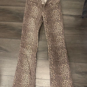 Leopardmönstrade bootcut byxor - Säljer ett par bruna bootcut byxor med leopardmönster. Byxorna har normal passform och är tillverkade i ett mjukt bomullsmaterial. Perfekta för dig som vill sticka ut med ett djuriskt mönster.
