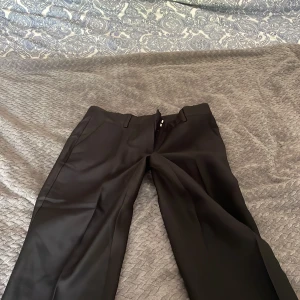 Svarta kostymbyxor med raka ben - Snygga svarta kostymbyxor med klassisk passform och raka ben. Byxorna har diskreta fickor både fram och bak samt hällor för bälte. Perfekta för en stilren look.