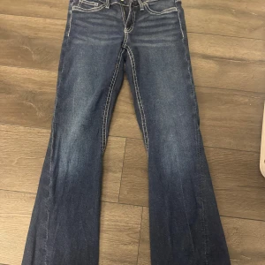 Mörkblå bootcut jeans med kontrastsömmar - Säljer ett par mörkblå jeans med bootcut-modell och tydliga vita kontrastsömmar. Jeansen har klassiska fem fickor och låg midja. Perfekta för dig som gillar en retroinspirerad stil.