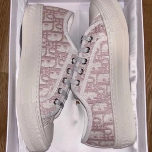 Rosa och vita sneakers från Dior - Säljer ett par snygga Dior sneakers i rosa och vitt med det klassiska Dior-mönstret. Skorna har vita snören, silverfärgade öljetter och en tjock vit sula. Perfekta för dig som vill ha något trendigt och exklusivt i garderoben.[Äkthetsbevis finns] [Dust bags etc finns] [Pris kan diskuteras]