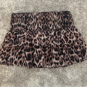 Leopardmönstrad volangkjol - Säljer en kort kjol med leopardmönster och volanger. Kjolen har smock i midjan för en bekväm passform och är tillverkad i ett lätt, luftigt material. Perfekt för dig som vill sticka ut med en trendig look.