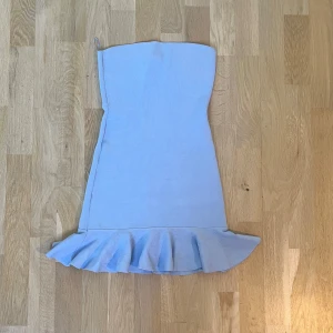 Ljusblå axelbandslös klänning från Zara - Säljer en ljusblå axelbandslös klänning från Zara med volangdetalj nertill. Klänningen har en figurnära passform och är perfekt för dig som vill ha en stilren och feminin look. Supersnygg till sommarens alla tillfällen!