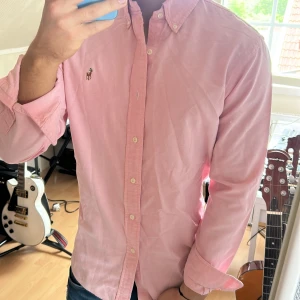 Rosa skjorta från Polo Ralph Lauren - Säljer en klassisk rosa skjorta från Polo Ralph Lauren i slim fit. Skjortan har knappar framtill, button-down krage och den ikoniska broderade loggan på bröstet. Perfekt för dig som gillar stilrena plagg med snygg passform.