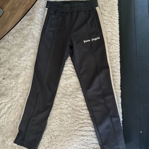 Gråa Palm Angels byxor  - Palm Angels gråa med vita revärer längs sidorna och logga tryckt på vänster lår. Byxorna har elastisk midja och raka ben, tillverkade i ett glansigt syntetmaterial. Perfekt för en avslappnad och trendig look på hösten till exempel. Dessa går för 4-5k nypris. Pris kan diskuteras.