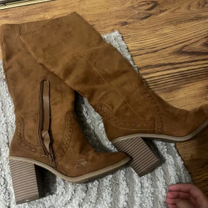 Bruna höga boots med klack från Time and Tru - Snygga bruna höga boots i mockaimitation med grov klack och dekorativa sömmar. Dragkedja på insidan för enkel påtagning. Perfekta för att lyfta din outfit med en trendig touch.