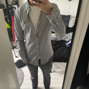 Randig skjorta från Polo Ralph Lauren - Snygg vit och blå randig skjorta från Polo Ralph Lauren i slim fit. Klassisk design med knappar framtill och broderad logga på bröstet. Perfekt för dig som gillar stilrena plagg med en sportig touch.