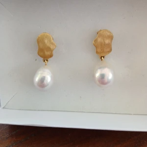 Enamel Copenhagen örhänge - Eleganta örhängen med oregelbunden guldpläterad platta och hängande vita barockpärlor. Perfekta för att ge en lyxig touch till din stil. Säljs som par.