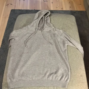 Ljusgrå kasmir hoodie - Säljer en enkel och stilren ljusgrå hoodie med huva och dragsko. Tröjan har långa ärmar och ribbade muddar vid ärmslut och nederkant. Perfekt för en avslappnad look.