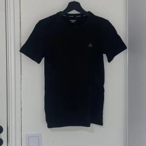 Svart t-shirt från Calvin Klein - Säljer en svart t-shirt från Calvin Klein med liten vit 'ck'-logga på bröstet. Klassisk rund halsringning och korta ärmar. Perfekt basic-plagg med stilren design och mjukt bomullsmaterial. Pris kan diskuteras