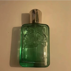 Greenley Eau de Parfum från Parfums de Marly - Greenley från Parfums de Marly är en lyxig parfym i en grön glasflaska med silverfärgat lock. Flaskan har en elegant design med ingraverade hästar och sköld. Kommer i originalkartong i matchande grön färg. Volym: 125 ml.