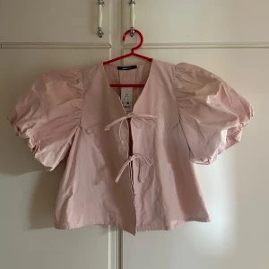 Ljusrosa puffärmad blus från Gina Tricot - Supersöt ljusrosa blus från Gina Tricot med puffiga korta ärmar och knytning framtill. Aldrig använd och har kvar prislappen på. Nypris 500kr🩷