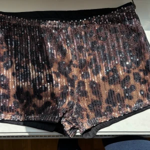 Glittriga leopardmönstrade shorts - Säljer ett par korta shorts med leopardmönster och massor av paljetter som ger en riktigt glittrig look. Perfekta för dig som vill sticka ut! De har en normal passform och är i syntetmaterial.