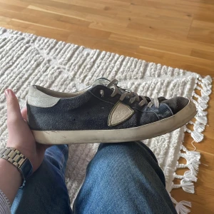 Phillipe model - Säljer ett par svarta sneakers från Philippe Model med vita detaljer på häl och sula. Skorna har snörning, rund tå och platt sula. Klassisk design med märkets logotyp på sidan och kontrastfärgade partier.