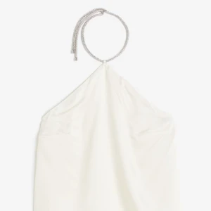 Vit halterneckblus med glittrigt band - Säljer en elegant vit halterneckblus med ett glittrigt, silverfärgat band som knyts runt halsen. Blusen har en slät och mjuk yta, perfekt för dig som vill sticka ut med stilrena detaljer.