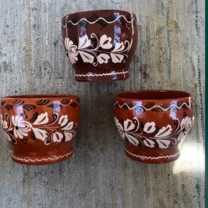 3 signerade krukor  - Bilderna visar tre handmålade blomkrukor med traditionellt blommönster i vitt och svart på rödbrun botten. Blomkrukorna har en rustik känsla och passar perfekt för dig som gillar unika och dekorativa föremål till hemmet. Perfekta att ha växter i eller som prydnad
