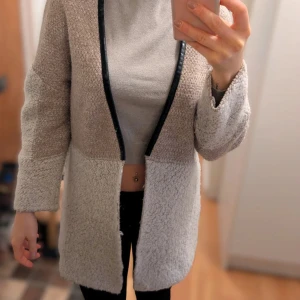 Beige teddyjacka från Mango - Säljer en beige teddyjacka från Mango med öppen front och svarta kantdetaljer. Jackan har lång ärm och är tillverkad i ett mjukt, teddy-liknande material som ger en mysig känsla. Perfekt för lager-på-lager-stil under kyliga dagar.