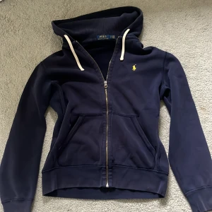 Mörkblå kofta från Polo Ralph Lauren - Säljer en mörkblå hoodie/kofta från Polo Ralph Lauren med dragkedja och vit snörning i huvan.💕storlek S