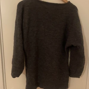 Mörkgrå ull tröja från Indiska - Mysig mörkgrå ull tröja från Indiska med enkel design och rund halsringning. Tröjan har långa ärmar och är perfekt för kyligare dagar. Passar dig som gillar en klassisk och stilren look. obs: har ändrat formen på tröjan, sömnen syns ej