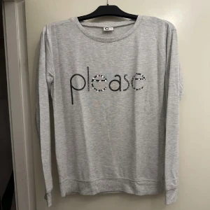 Ljusgrå sweatshirt - Ljusgrå sweatshirt med trycket 'please' i svart och mönstrade bokstäver framtill. Tröjan har rund halsringning och långa ärmar. Perfekt för en avslappnad stil. Passar även om man har storlek M. Oanvänd. 