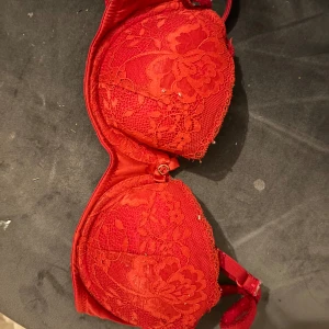 Röd spets-bh med rosett - Säljer en röd bh med vacker spets och liten rosett framtill. Bh:n har justerbara axelband och vadderade kupor för extra stöd. Perfekt för dig som vill ha något snyggt och bekvämt under kläderna.