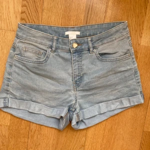 Ljusblå jeansshorts från H&M låg midja - Ljusblå jeansshorts från H&M med klassisk femficksdesign och uppvikta benslut. Shortsen har normal passform men lågmidjade och stängs med knapp och dragkedja. Perfekta för varma dagar och enkel att matcha med olika toppar. Trendiga!