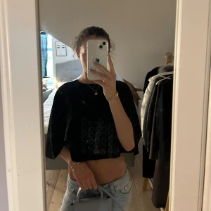 Svart croppad blus med vida ärmar - Säljer en svart croppad blus med vida, korta ärmar och lös passform. Toppen har en stilren design utan synliga detaljer och är perfekt för en trendig look. Passar till både jeans och kjol och perfekt nu till sommar kvällar☀️☀️ Nypris: 549,95kr