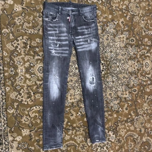 Grå Svarta (Slim Fit) jeans från Dsquared2 - Säljer ett par Grå Svarta skinny jeans från Dsquared2 med slitningar och distressed detaljer. Byxorna har fem fickor, dragkedja och knapp, samt Dsquared2-logga på röd etikett. Snygg tvätt med vita partier och färgstänk.