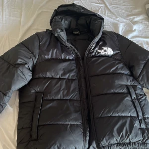Svart pufferjacka från The North Face - Säljer en svart pufferjacka från The North Face med huva och dragkedja. Jackan har två sidofickor och logga på bröstet samt ryggen. Perfekt för kyliga dagar och riktigt skön att bära.(kan också prata om och sänka priset)