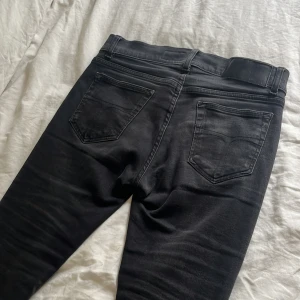 Svarta slim jeans Tiger of Sweden - Svarta jeans från Tiger of Sweden i slim fit-modell. Klassisk femficksdesign med snygga detaljer och diskret tvätt. Jeansen är tillverkade i ett stretchigt bomullsmaterial som sitter tajt men bekvämt. Perfekta för dig som gillar en stilren och modern look. De är i storlek 28/32 men kan passa på 28/30